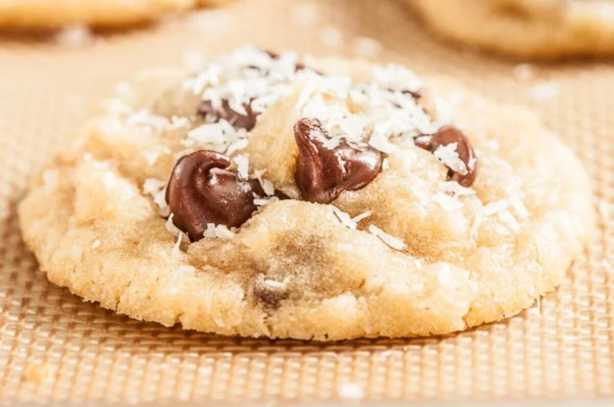 Close-up of an Easter chocolate chip cookie sprinkled with shredded coconut on a textured surface.