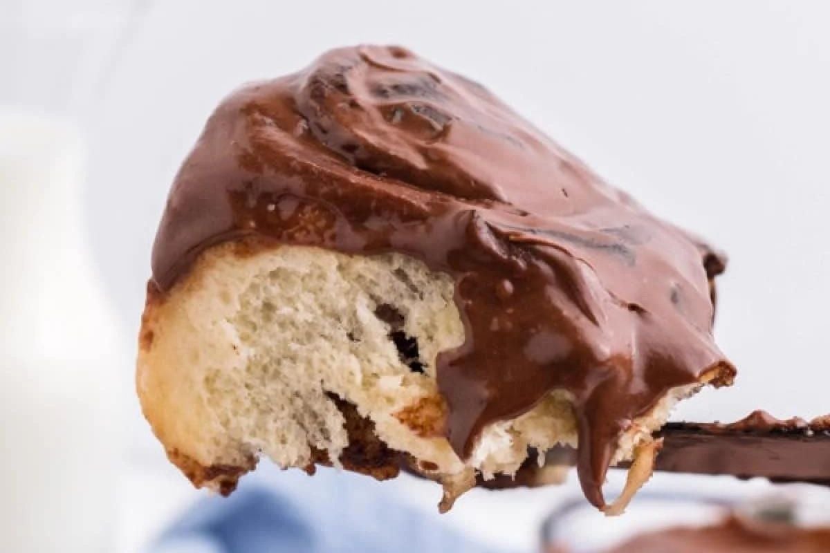 A close-up of a partially eaten chocolate-covered cinnamon roll on a fork.