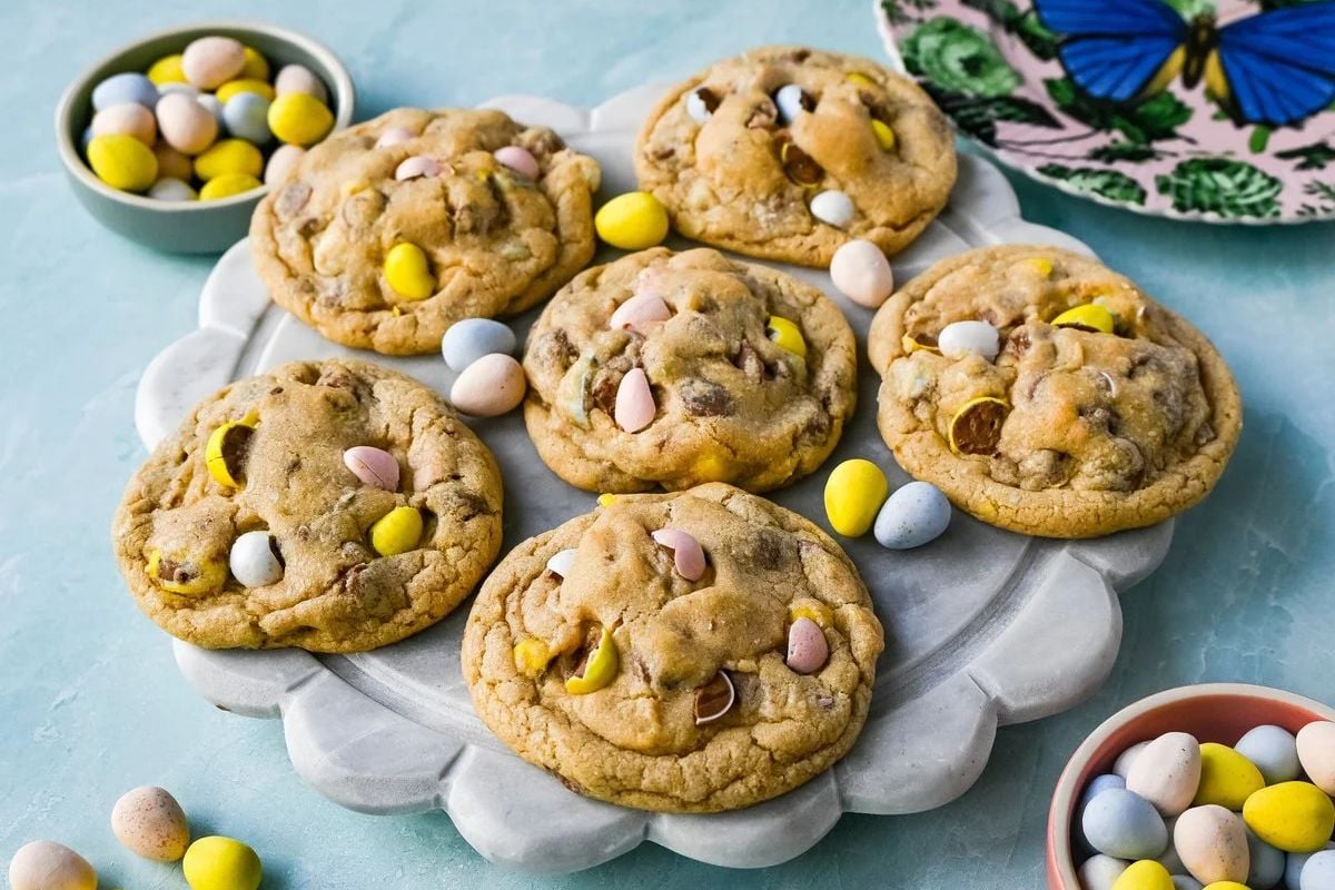Plate of homemade Easter cookies with colorful candy pieces, surrounded by extra candies on a light blue surface.