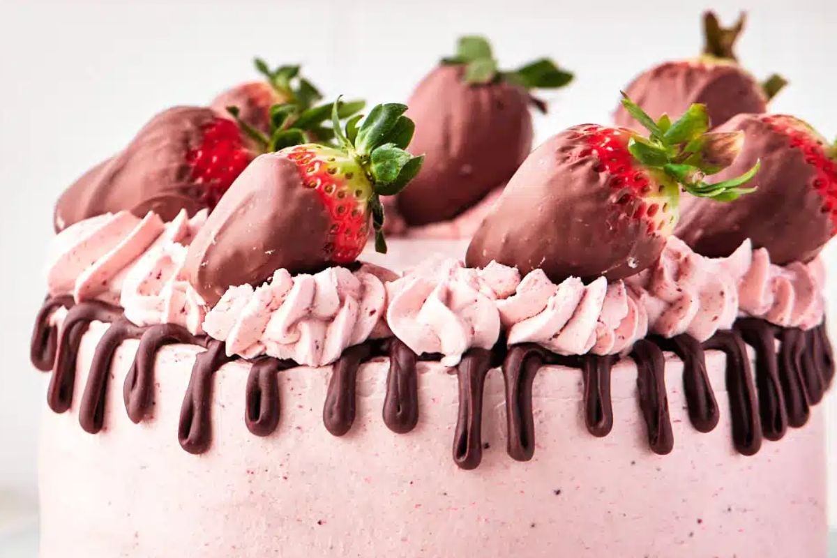 A strawberry layer cake decorated with chocolate-dipped strawberries, whipped cream, and chocolate drizzle.