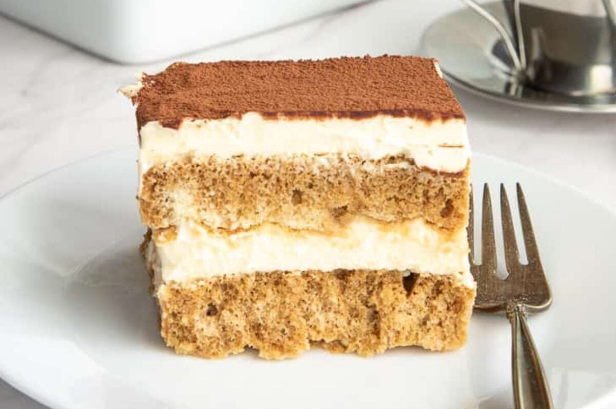 A slice of tiramisu layer cake on a white plate with a fork.