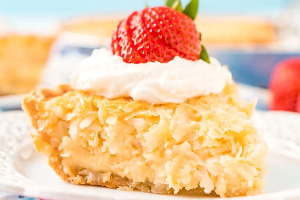 A slice of coconut cream pie topped with whipped cream and a fresh strawberry on a white plate, perfect for Easter desserts.