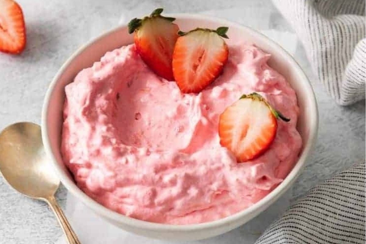 Strawberry jello salads in a bowl with a spoon.
