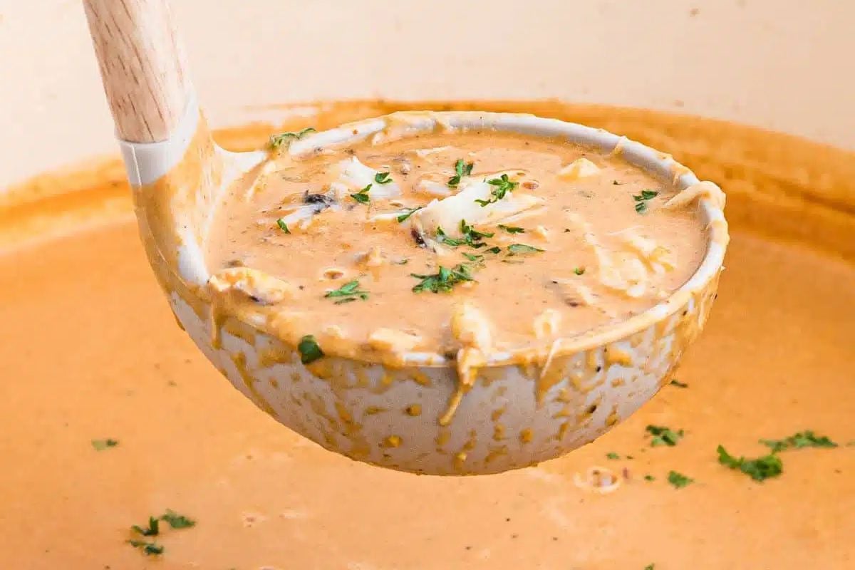 A ladle scooping up creamy seafood soup garnished with herbs from a pot.