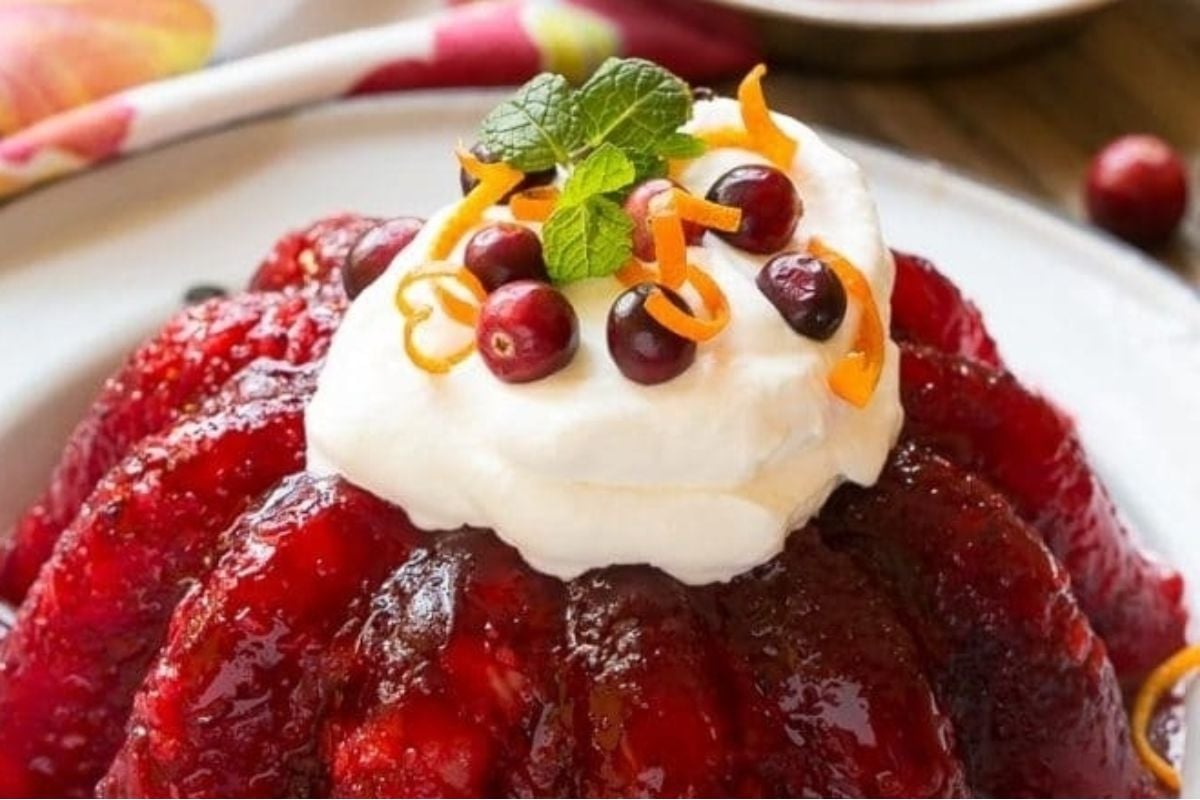 A cranberry jello salad topped with whipped cream and oranges.