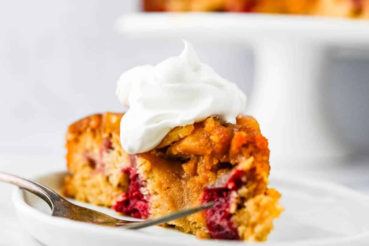 A slice of berry upside down cake topped with whipped cream on a plate with a fork.