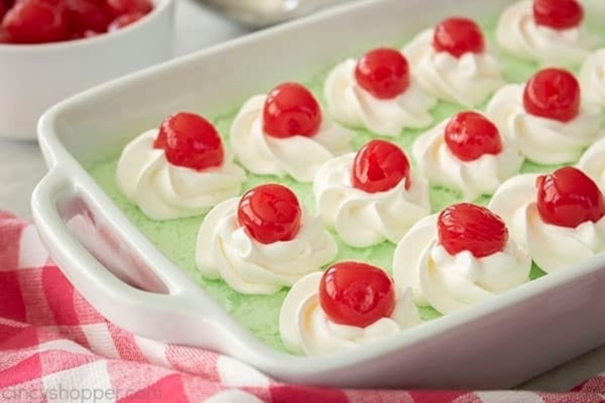 A white dish with whipped cream, cherries, and jello salads on top.