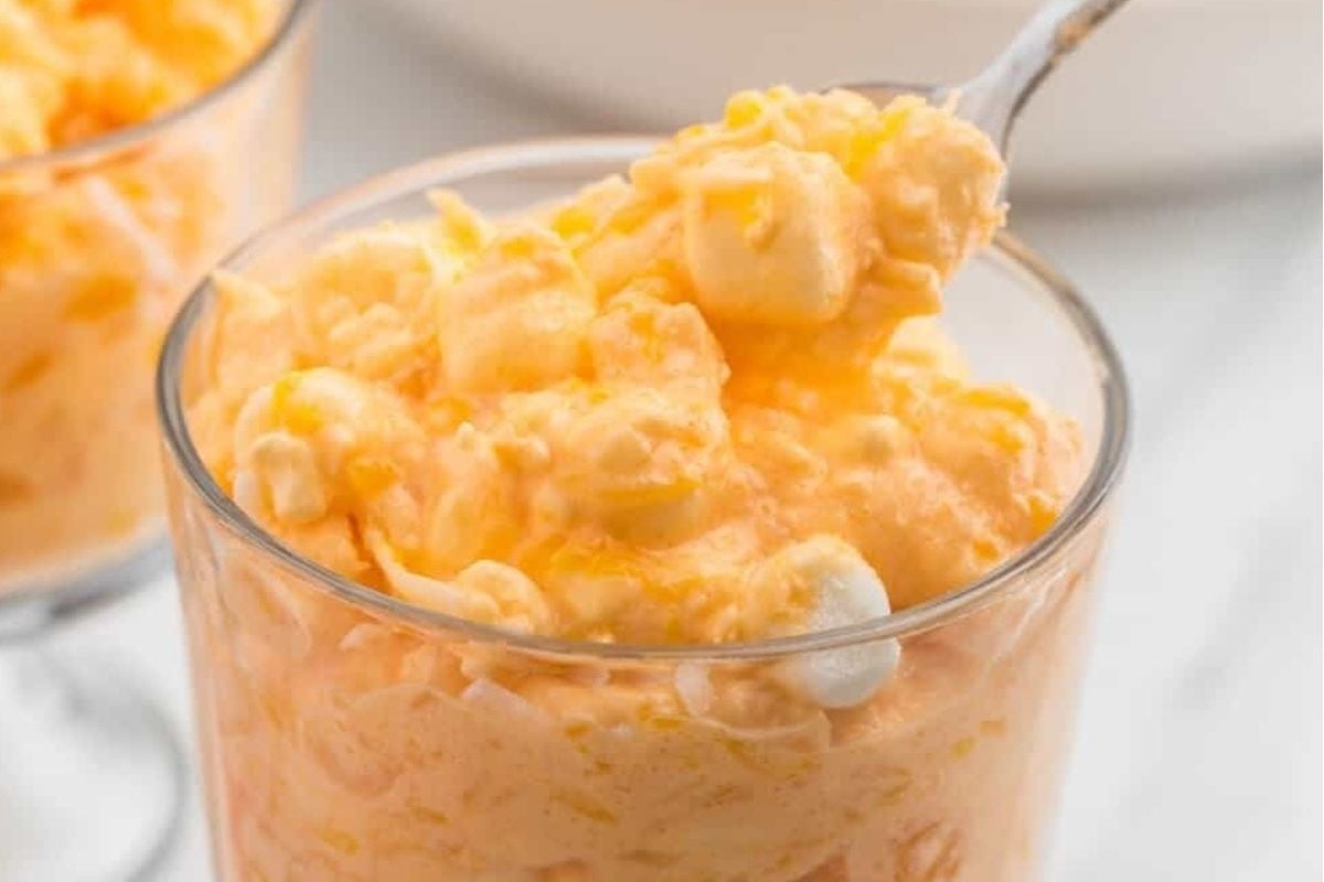 A spoonful of orange jello salad in a glass.