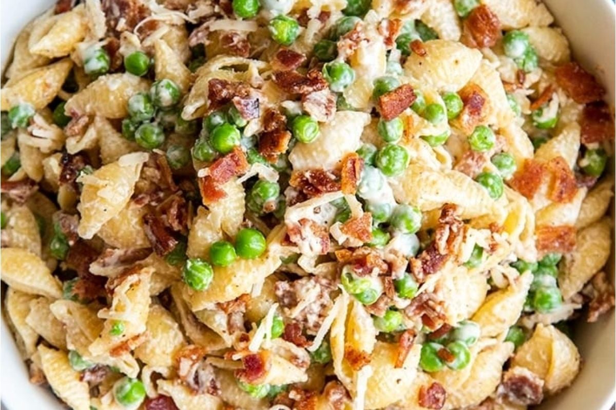 Pea pasta with bacon and peas in a white bowl, perfect for potluck sides.