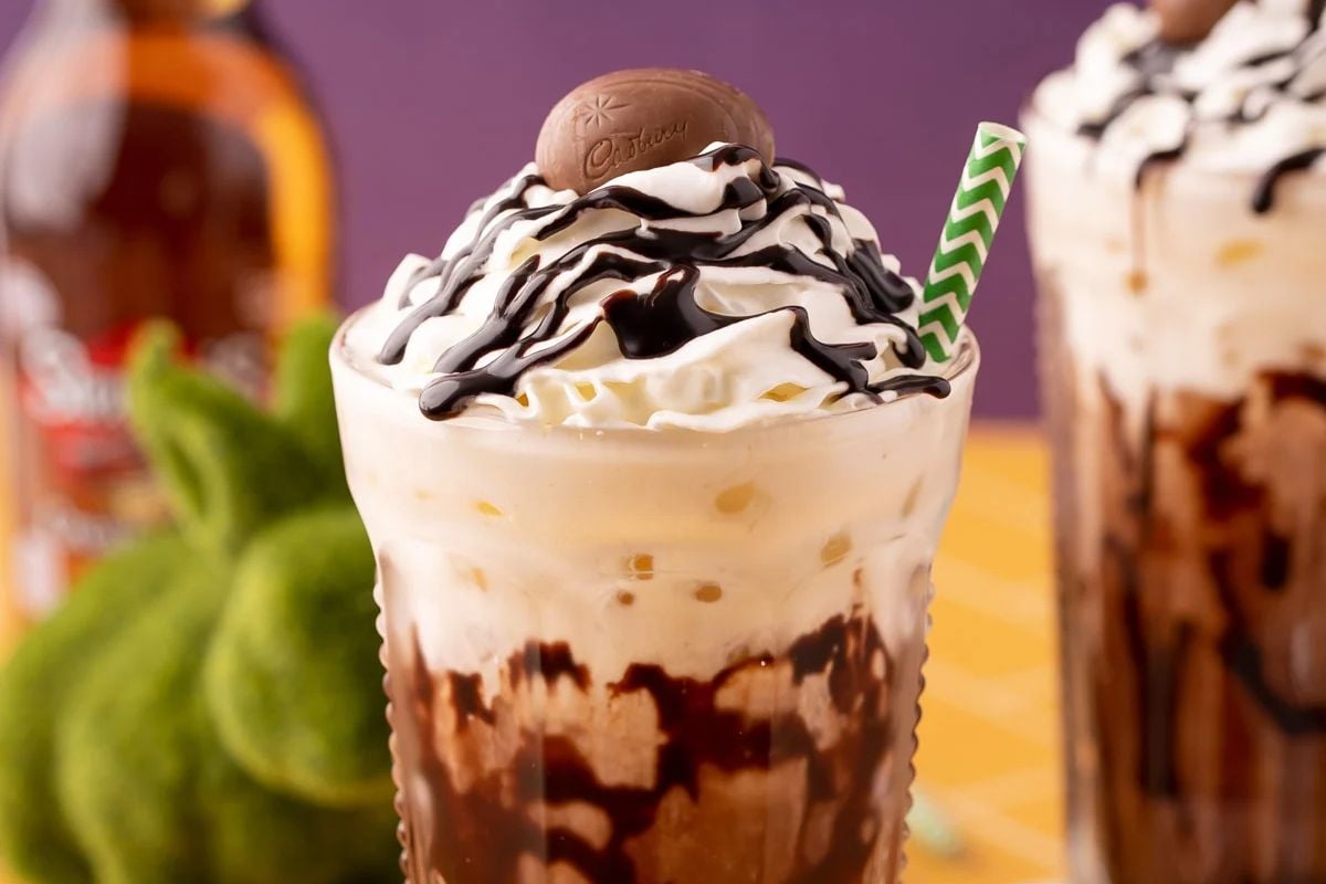 Two creamy Easter milkshakes topped with whipped cream, drizzled with chocolate sauce, and garnished with a chocolate candy, presented with a striped straw.