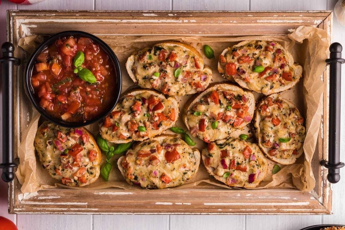 Tray of baked stuffed mushrooms with a side of cheesy tomato sauce.
