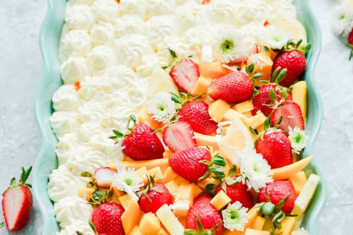 A colorful fruit platter with strawberries, kiwi, and cantaloupe garnished with whipped cream, perfect for Easter cakes.