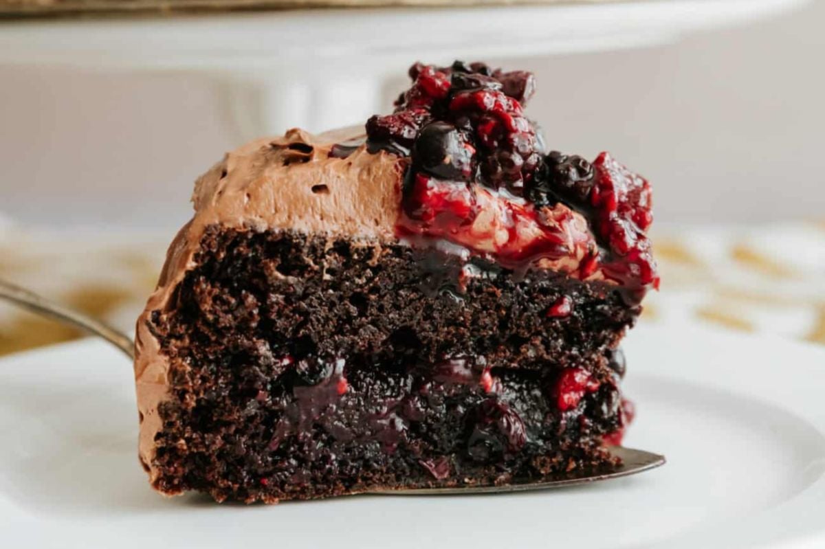 A slice of chocolate layer cakes topped with berry compote on a plate.