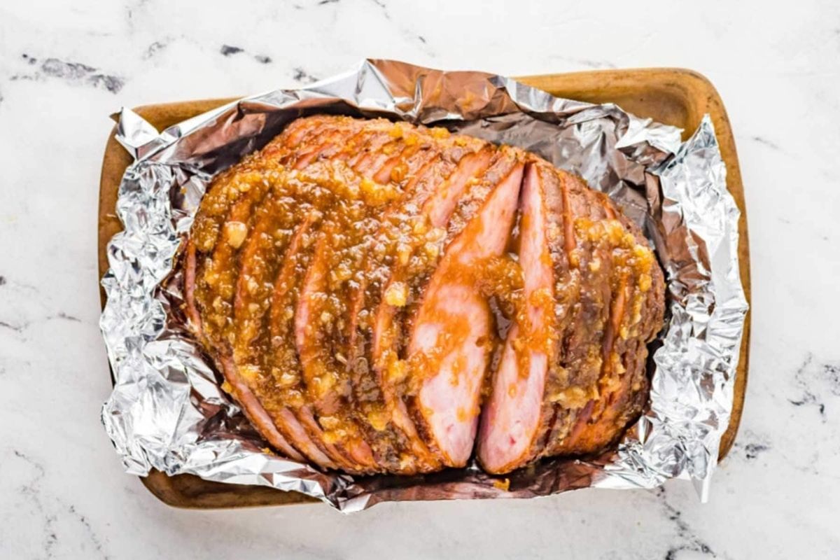 A ham wrapped in foil on a marble countertop, ready for slow cooker recipes.