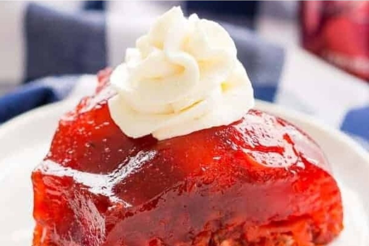 A slice of strawberry rhubarb pie on a plate, next to a serving of jello salads.