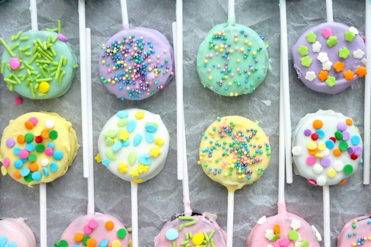 Assorted colorful frosted cake pops decorated with Oreo desserts and sprinkles.