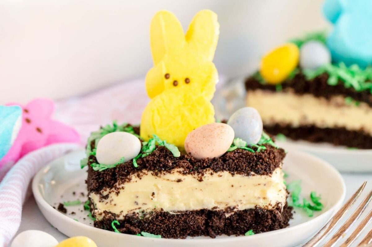 A slice of Easter cakes with a yellow bunny-shaped marshmallow on top, surrounded by candy eggs and colorful marshmallow chicks.