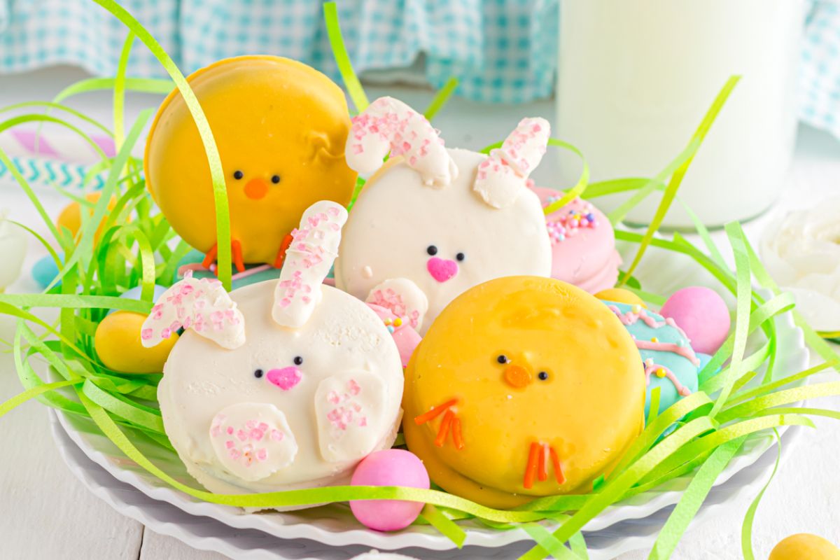 Colorful Easter-themed cake pops decorated to look like chicks and bunnies, presented in a festive setting with decorative grass, eggs, and Easter cookies.