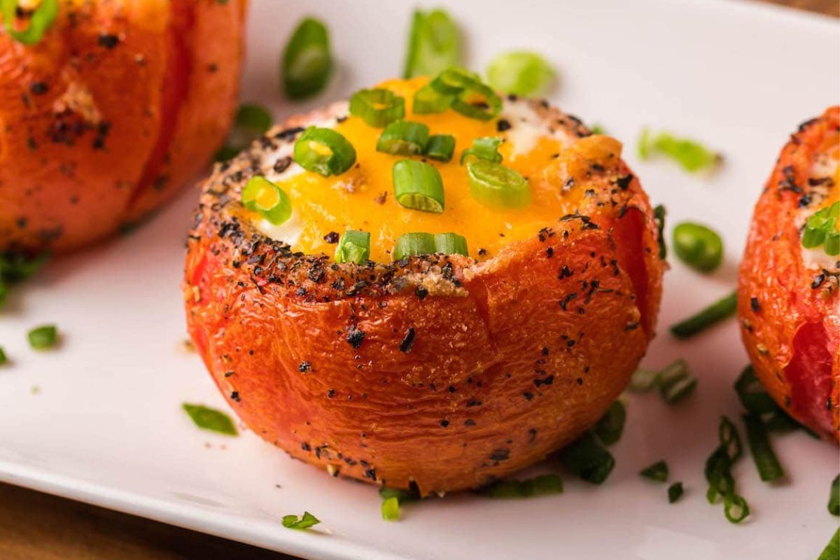 Stuffed tomatoes with cheese, egg recipes, and green onions on a white plate.