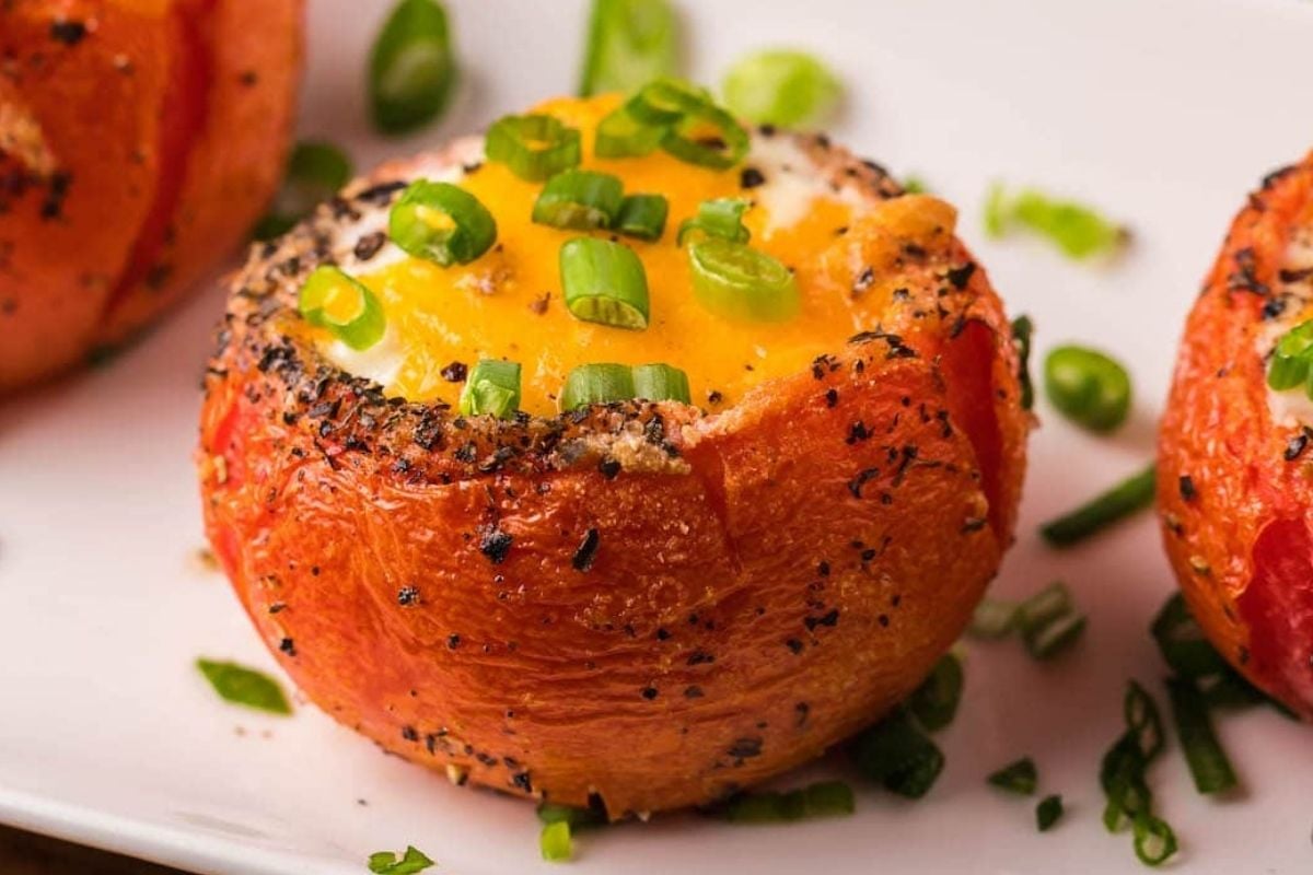 Baked tomatoes filled with eggs, topped with cheese and garnished with chopped green onions and black pepper, perfect for Father's Day breakfast.
