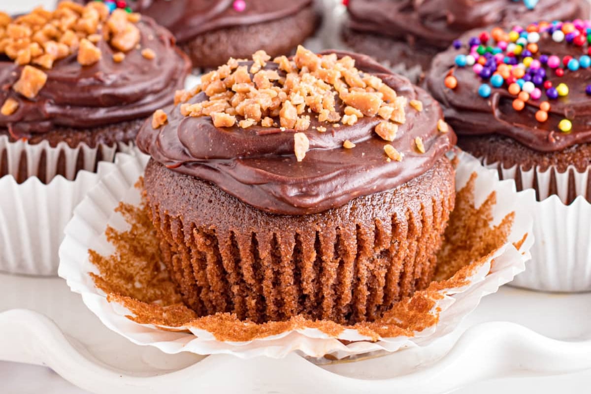 Chocolate poke cake cupcakes with various toppings on a white surface.