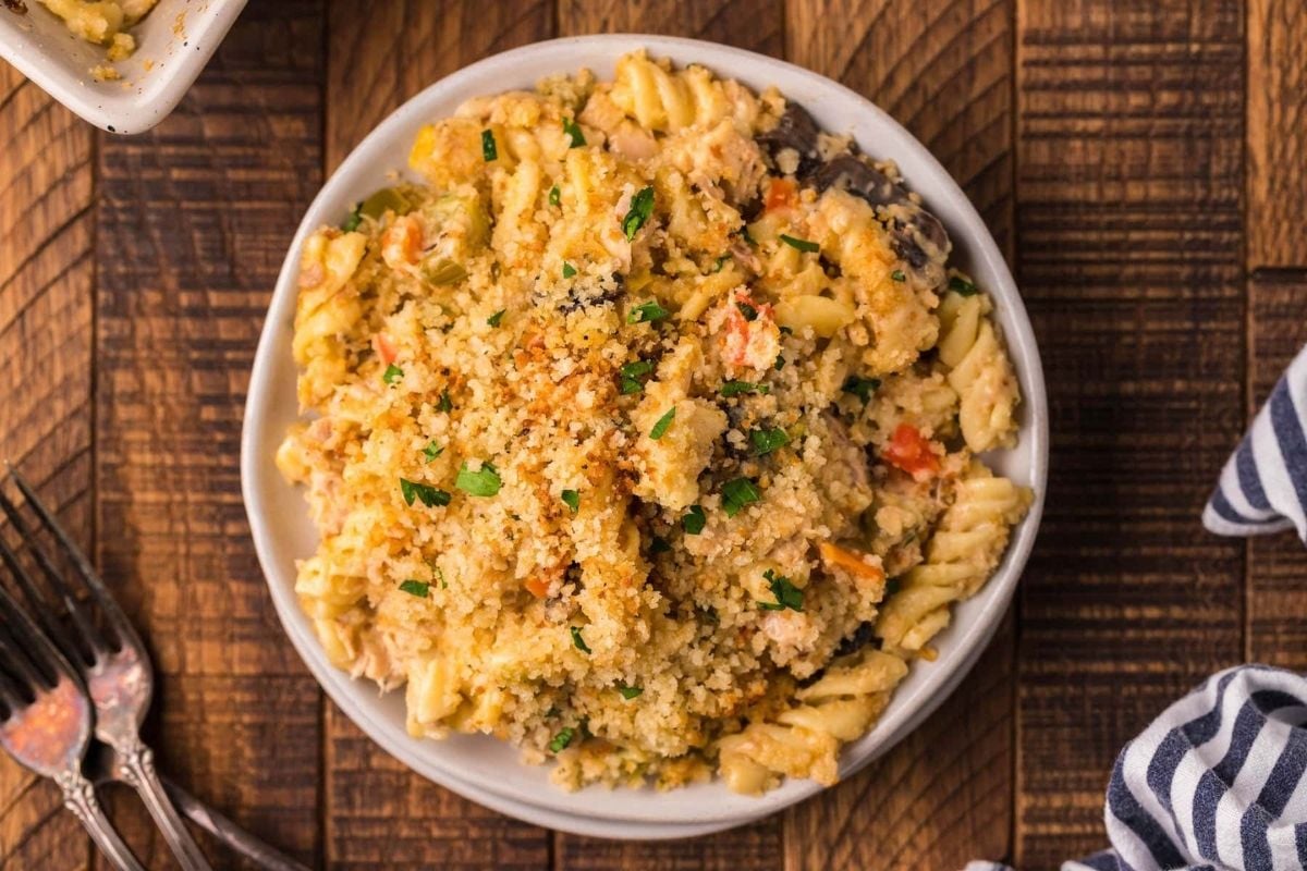 A bowl of creamy, cheesy pasta topped with herbs and breadcrumbs, served on a wooden table.
