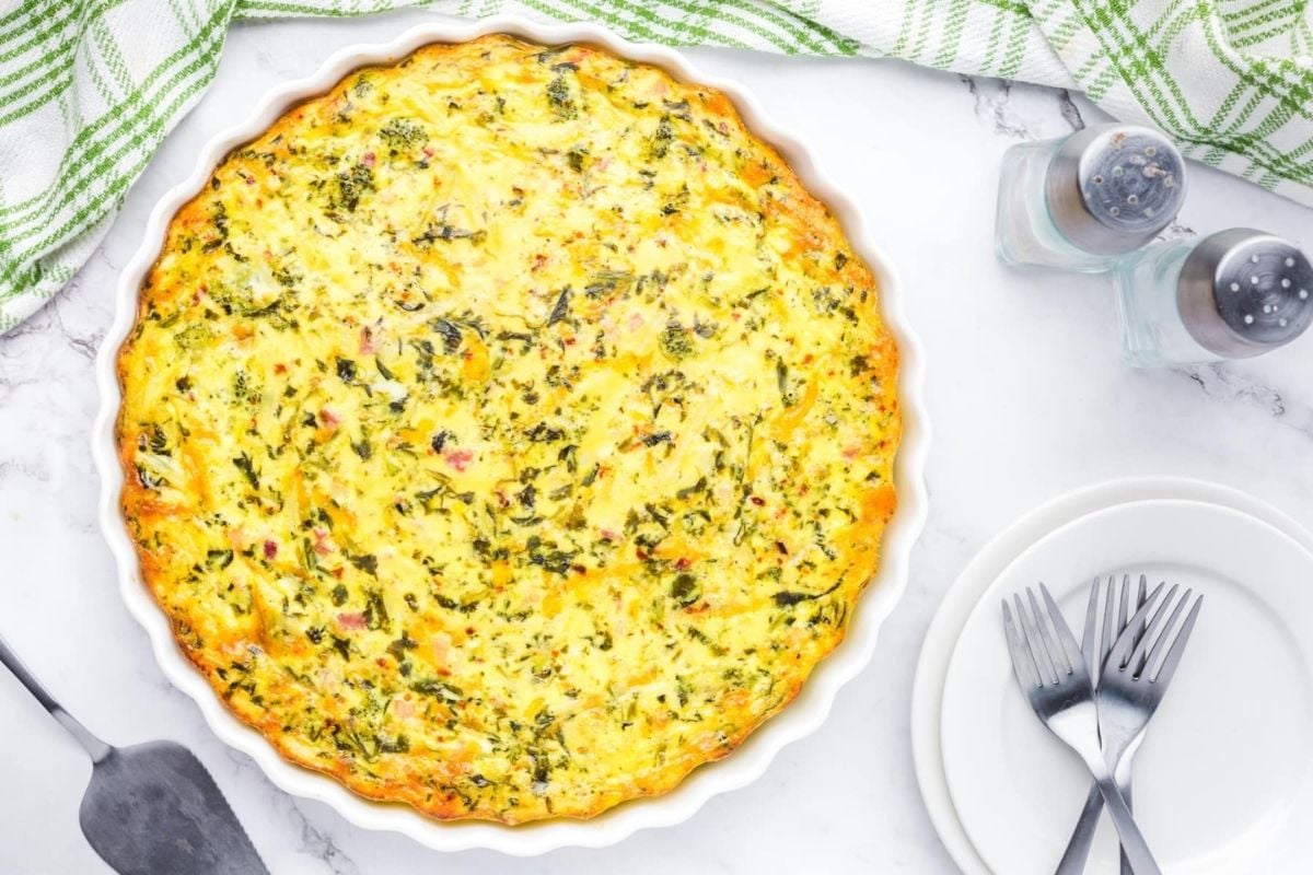 A freshly baked quiche for Father's Day breakfast on a marble countertop, accompanied by salt and pepper shakers and an empty plate with utensils.