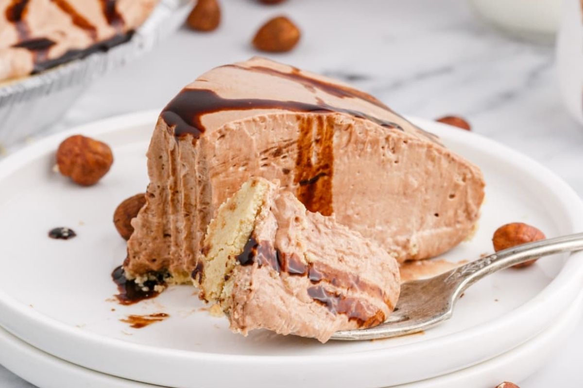 A slice of creamy chocolate almond mousse pie with a bite taken out, displayed on a white plate with whole almonds scattered around.