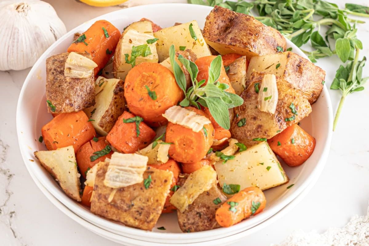 A bowl of potato recipes featuring roasted potatoes and carrots garnished with herbs.