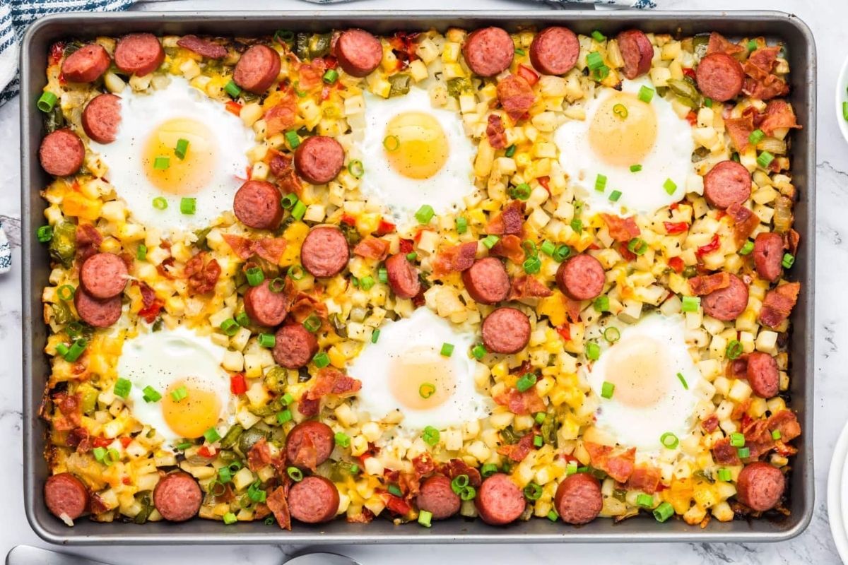 Father's Day breakfast sheet pan with diced potatoes, chopped vegetables, sliced sausages, and baked eggs.