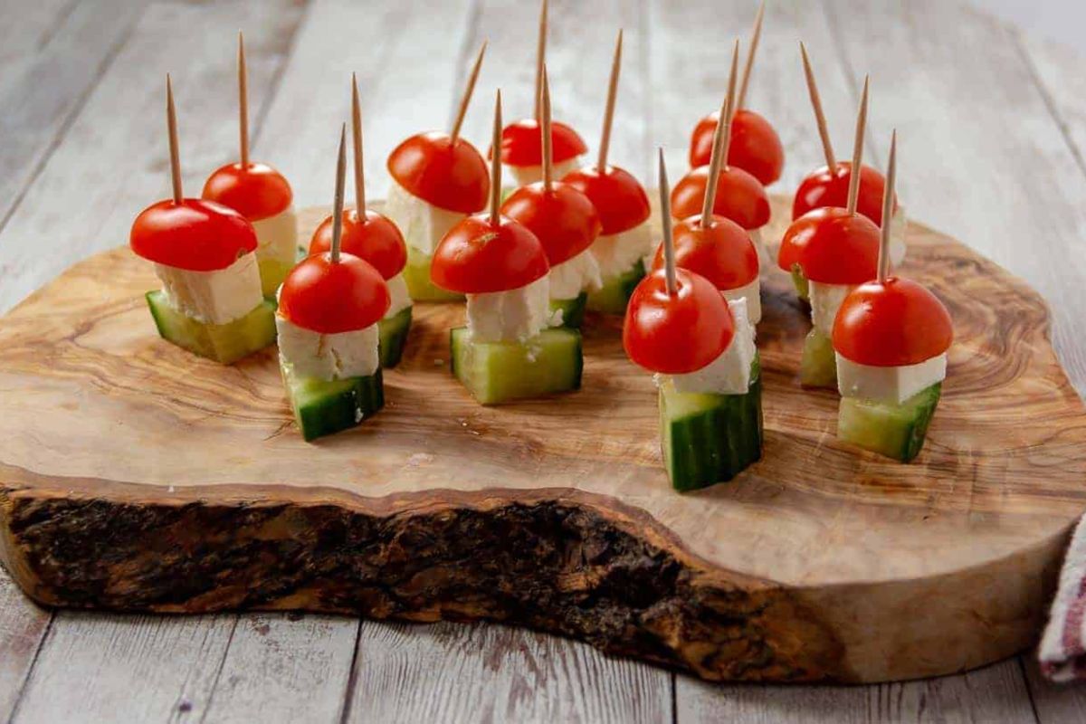 An Easter appetizer platter of cherry tomato and cucumber appetizers with mozzarella and toothpick skewers, served on a wooden board.