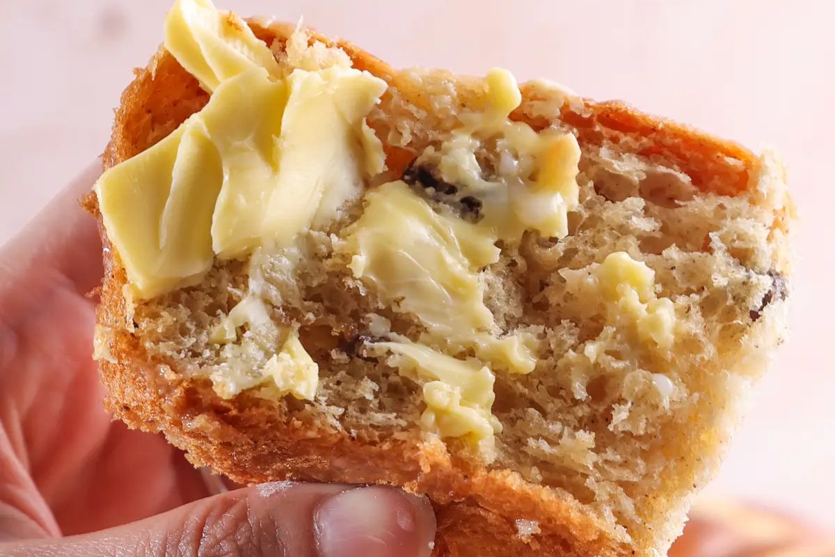 A close-up of a hand holding a piece of bread with chunks of fruit and melted butter on top, perfect for Easter sides.