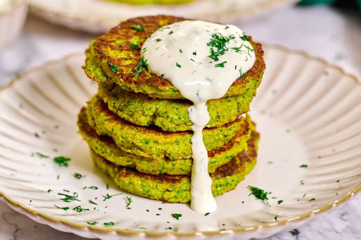A stack of green vegetable patties topped with a dollop of white sauce and garnished with fresh herbs, served on a white plate as Easter sides.