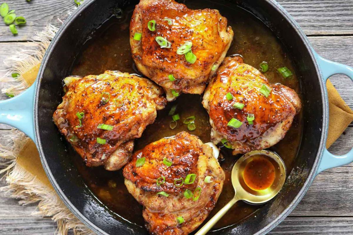 Glazed chicken thighs garnished with green onions in a cast-iron skillet for Easter dinner.
