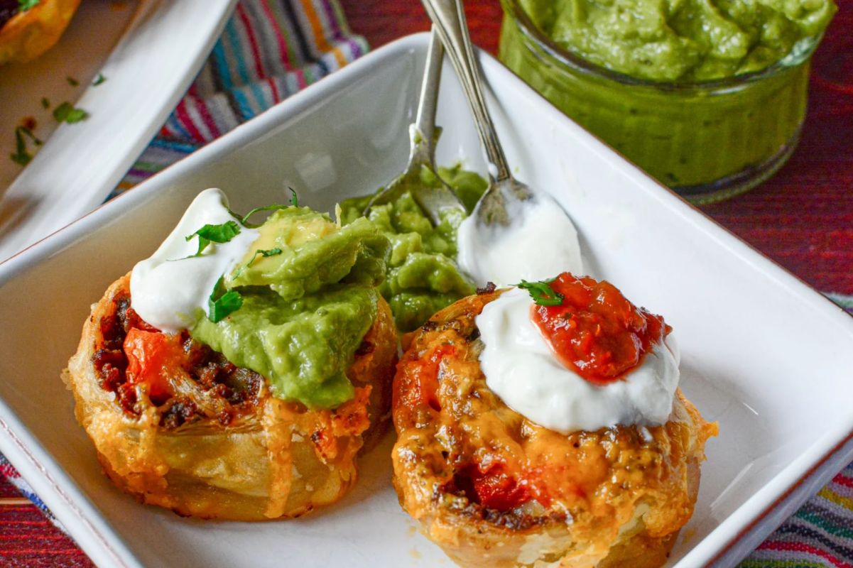 Two savory pastry cups topped with melted cheese, sour cream, and a dollop of guacamole on a white plate, perfect for a kids birthday party.