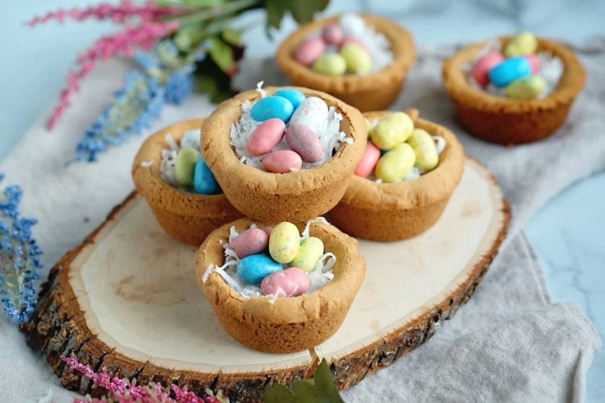 Easter cookies shaped like nests filled with colorful candy eggs on a wooden surface.