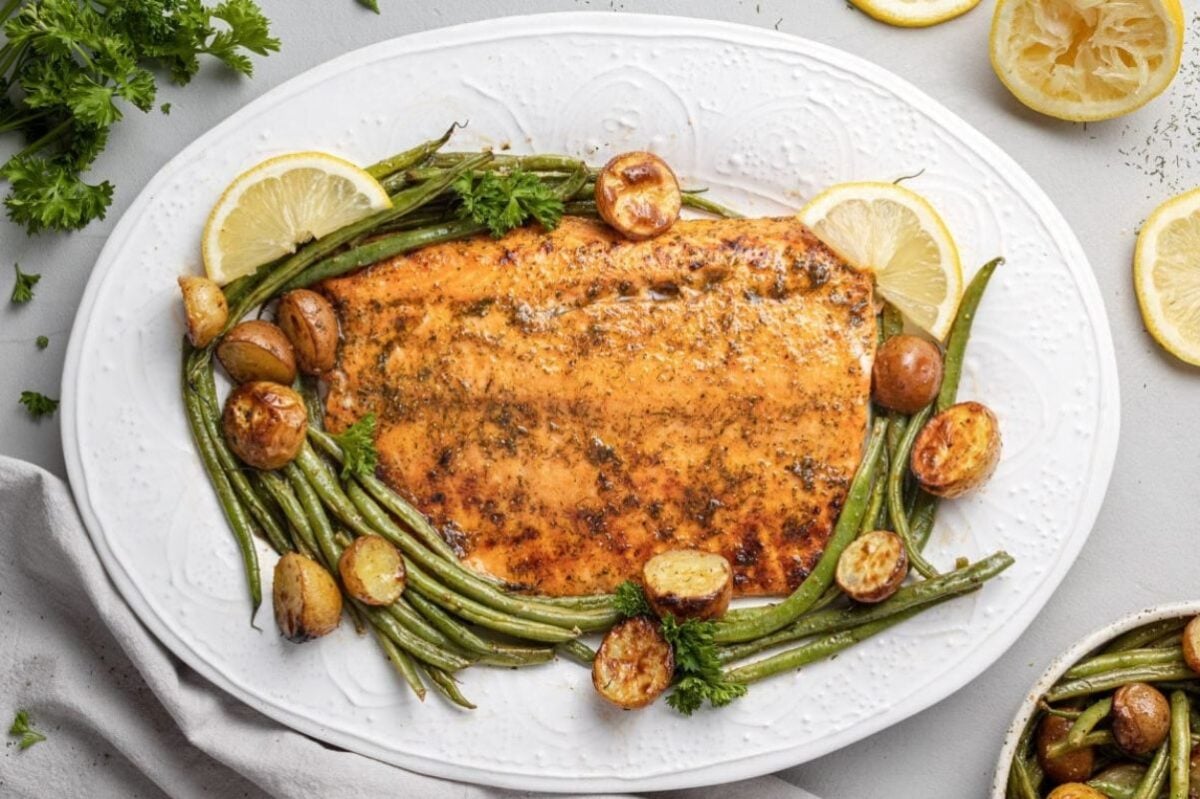 Grilled salmon fillet served with green beans, lemon slices, and roasted potatoes on a white plate, garnished with parsley. This dish is perfect for those who enjoy seafood recipes.