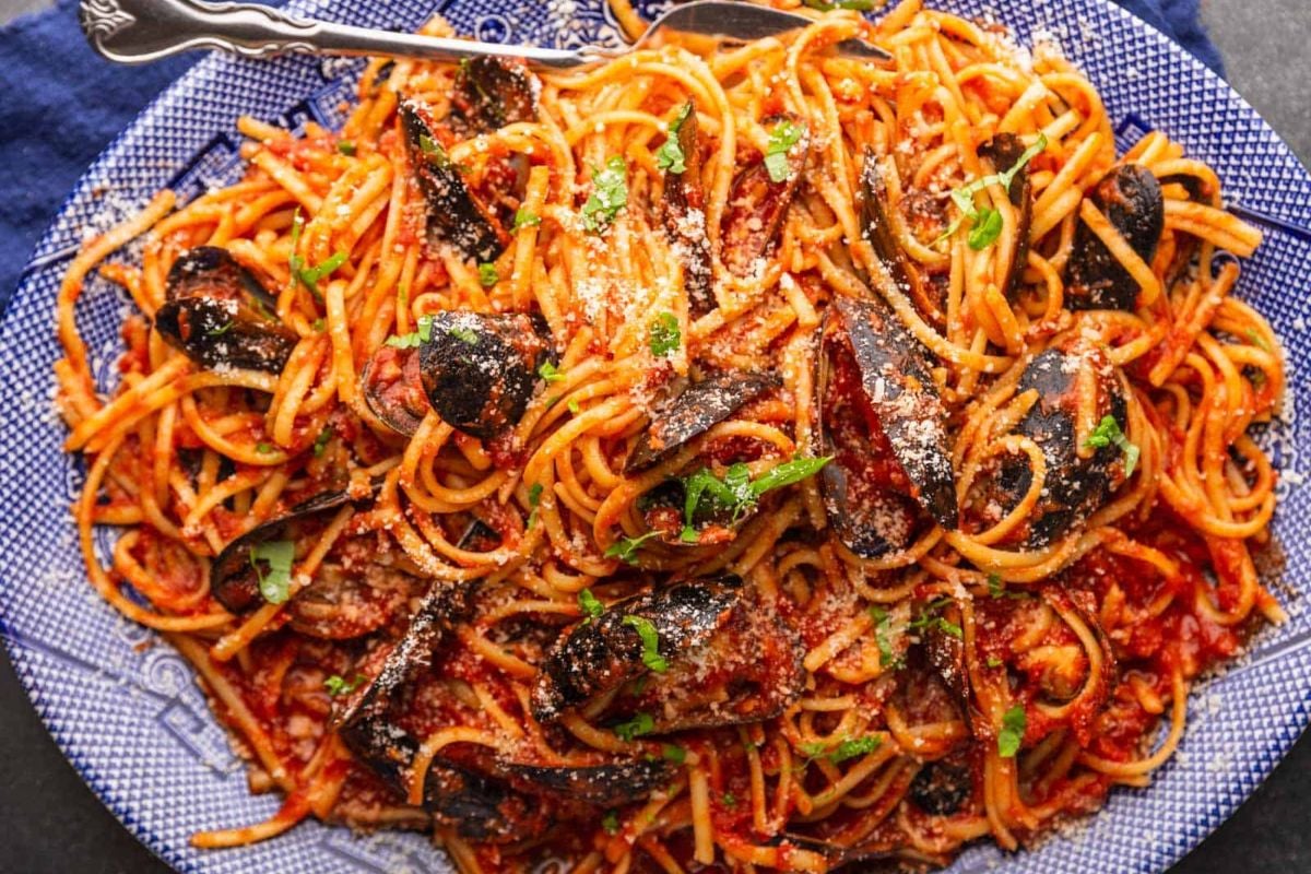 A plate of spaghetti with tomato sauce, sprinkled with parmesan cheese, garnished with basil leaves and black olives, featuring seafood, viewed from above.