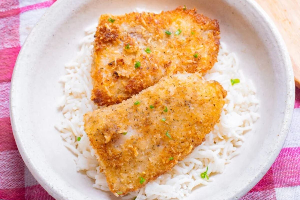 Two pieces of breaded seafood served on a bed of white rice, garnished with chopped green herbs, presented in a beige bowl.
