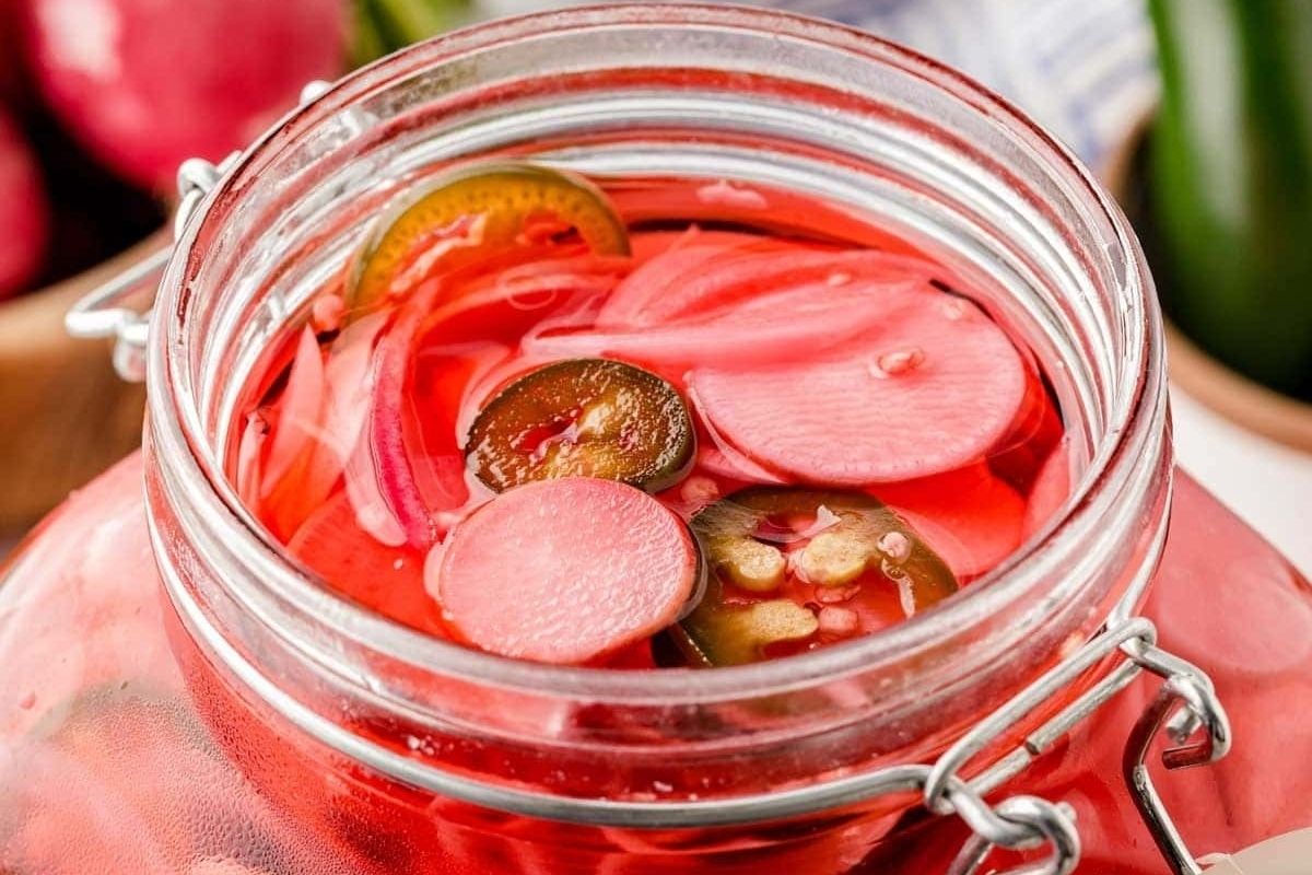 A jar of pickled radishes from our pickled recipes collection, with a lemon slice visible among the slices.