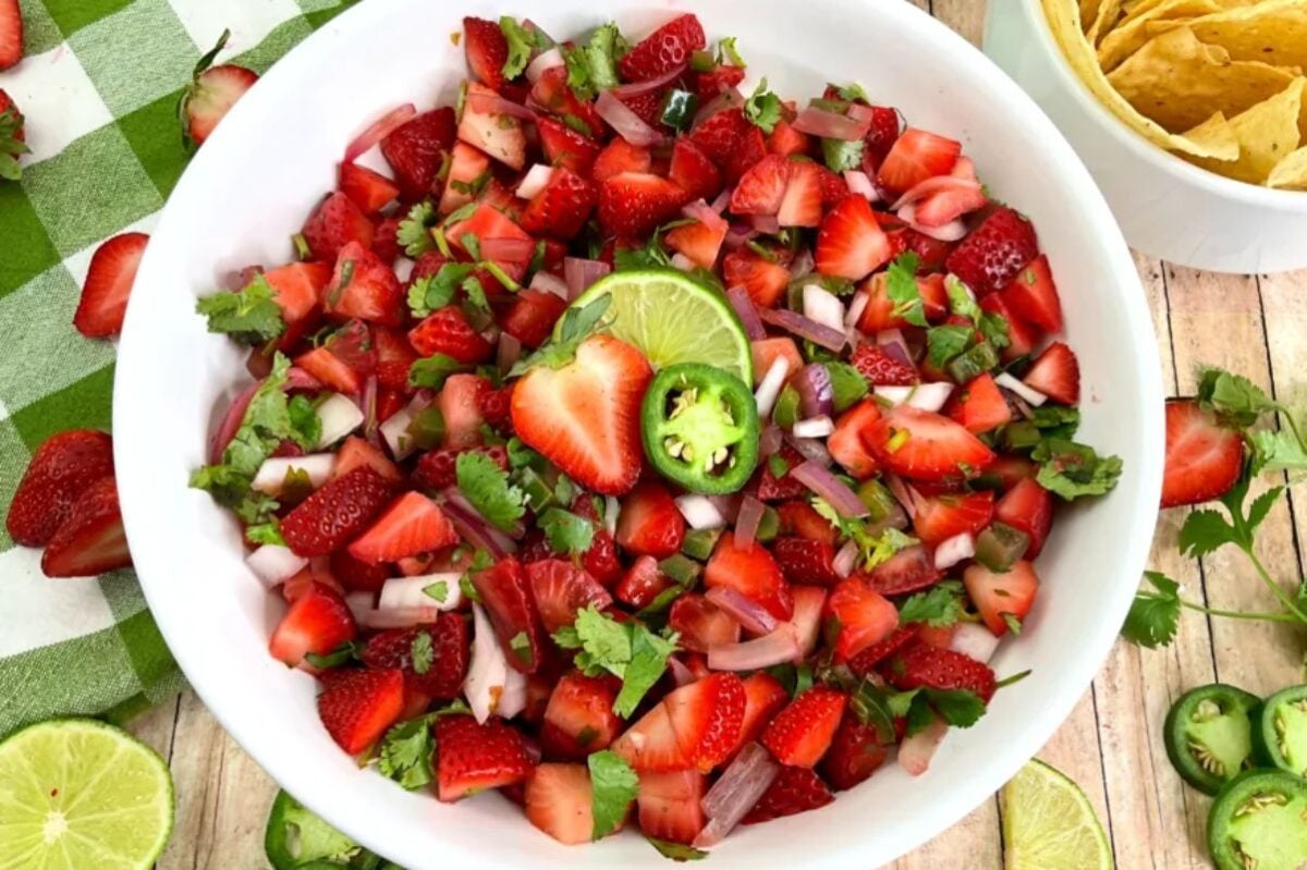 A bowl of strawberry salsa garnished with lime and jalapeño on a table with a napkin and tortilla chips on the side, serving as a festive Easter appetizer.