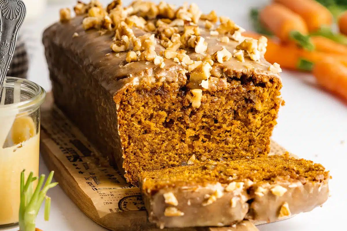 An Easter dessert featuring a moist carrot cake with cream cheese frosting and chopped nuts on top, with a slice taken out revealing its texture.