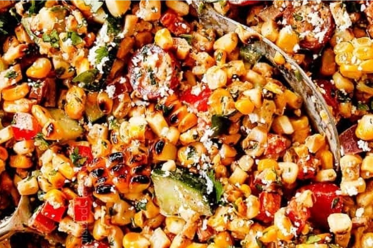 A bowl of corn and potluck sides with a spoon.