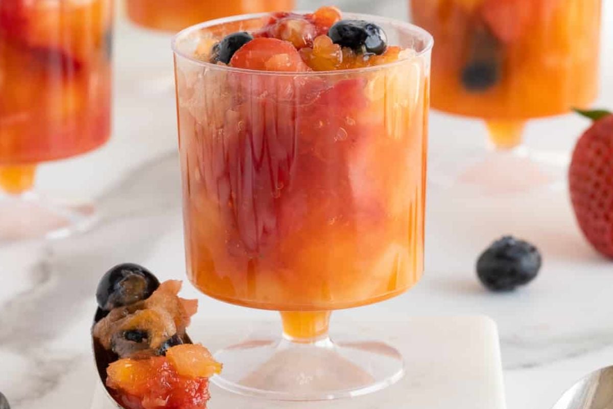 A glass filled with mixed fruit salad, including blueberries, strawberries, and diced fruit in syrup—perfect for single-serve individual desserts.