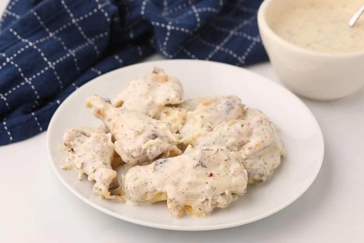 A plate of biscuits smothered in white gravy with pieces of chicken wings on a white tabletop.
