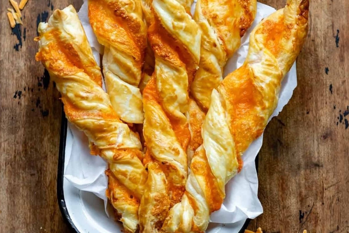 Golden cheese twists from cheesy recipes, made of puff pastry, displayed on a white plate.