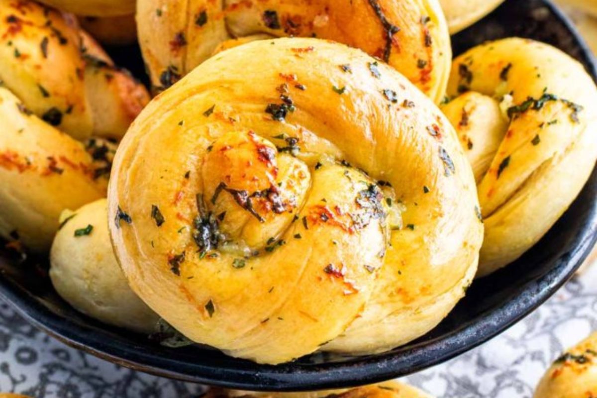 Freshly baked garlic knots garnished with herbs on a black plate, perfect as Easter sides.