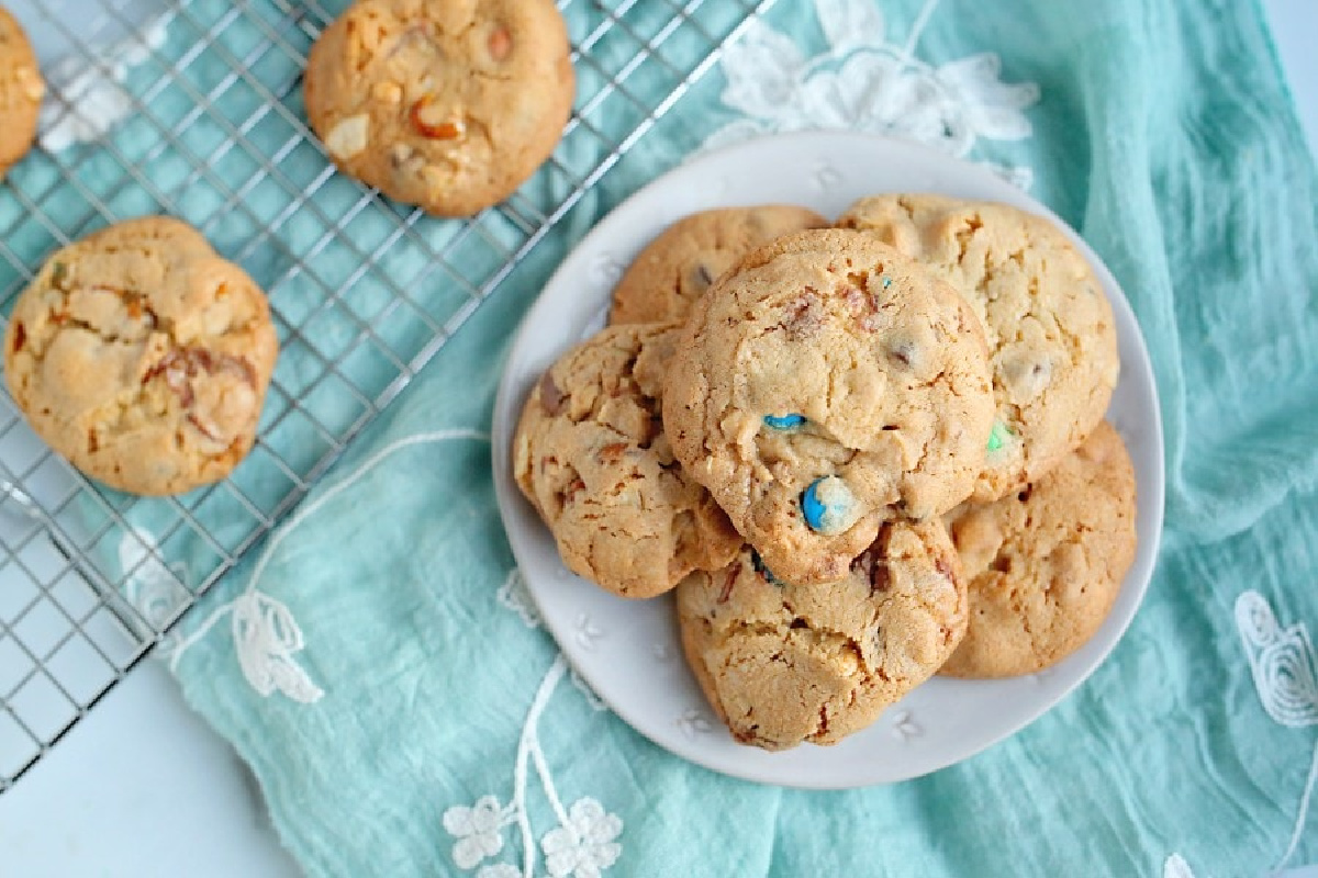 Freshly baked cookies with colorful chocolate candies served on a white plate, with additional cookies cooling on a wire rack in the background, following recipes from grandma.