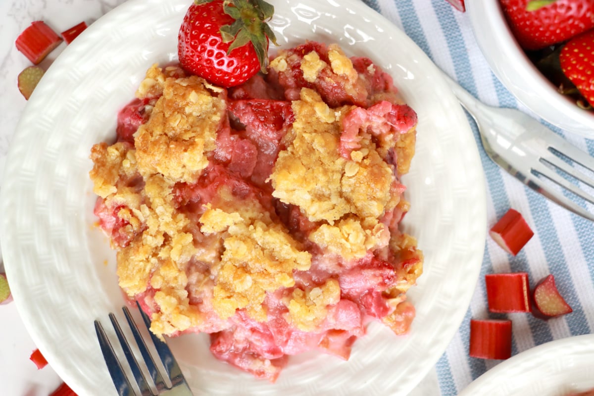 A serving of strawberry rhubarb crumble from grandma's recipes on a plate with fresh strawberries on the side.