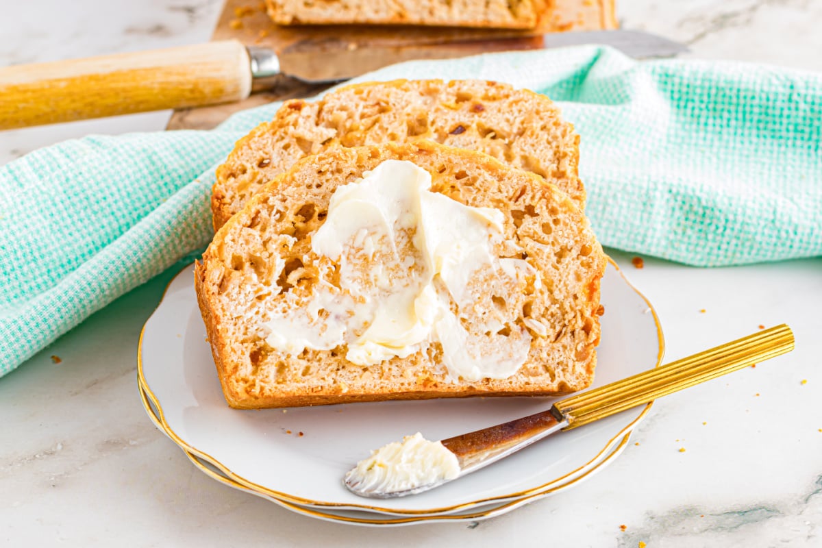 A slice of bread with butter on a plate, featuring a butter knife and a green cloth in the background, ready to be enjoyed with Grandma's recipes.